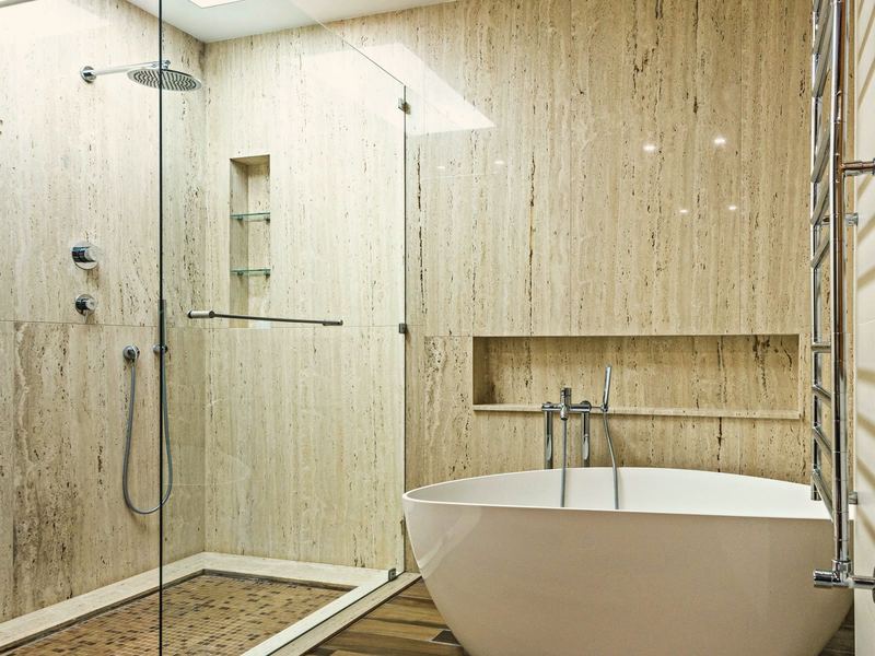 Traverten kaplı banyo, camlı duş, mozaik duş tabanı, gömme nişler ve oval küvet