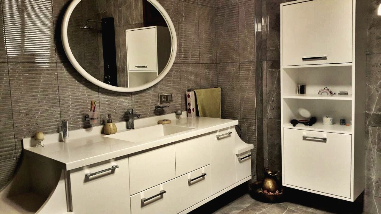 Yuvarlak aynalı lavabo tezgâhı, çizgili gri seramik duvar, açık raflı beyaz boy dolap