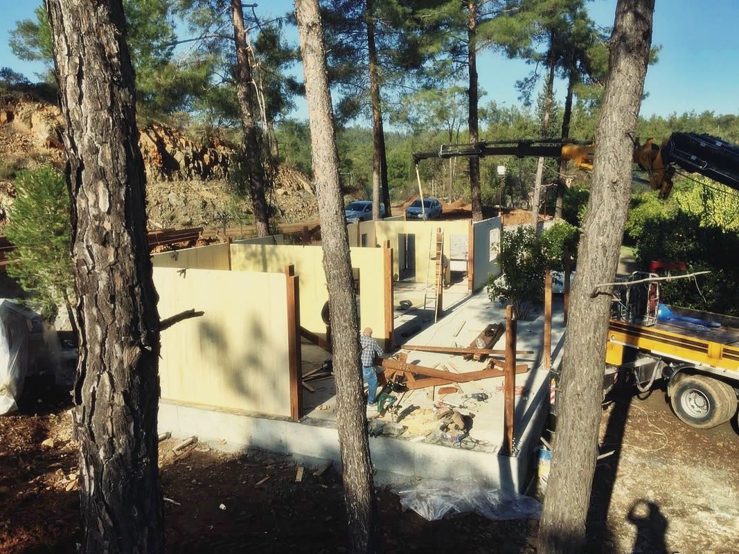Beton plak üzerinde ahşap panel duvarlar ve kolonlar, arkada vinç ve çam ağaçları