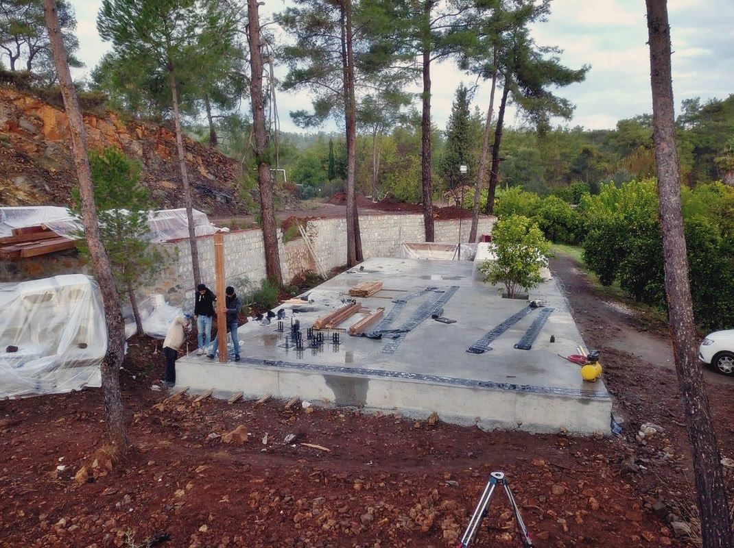 Taş istinat duvarı önünde beton temel plağı, ankraj bulonları ve siyah şeritler